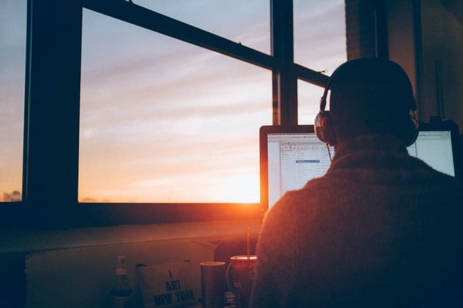 Person von hinten, die am Computer sitzt und Kopfhörer auf hat. 