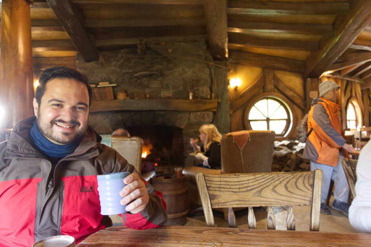 Sitzender Mann mit Becher in der Hand in einer Holzhütte