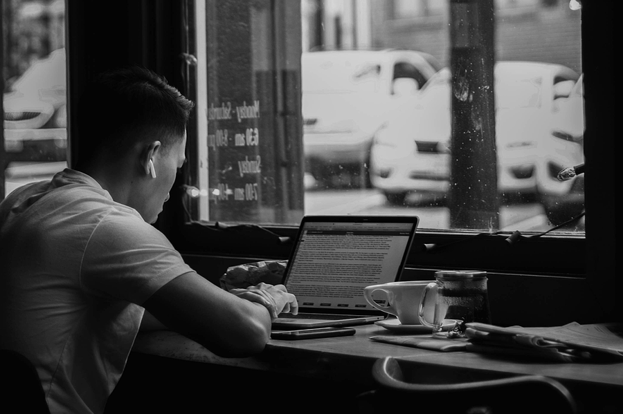 Ein Mann sitzt vor einem Laptop. Neben ihm steht ein Kaffe. Das Bild ist schwarz-weiß