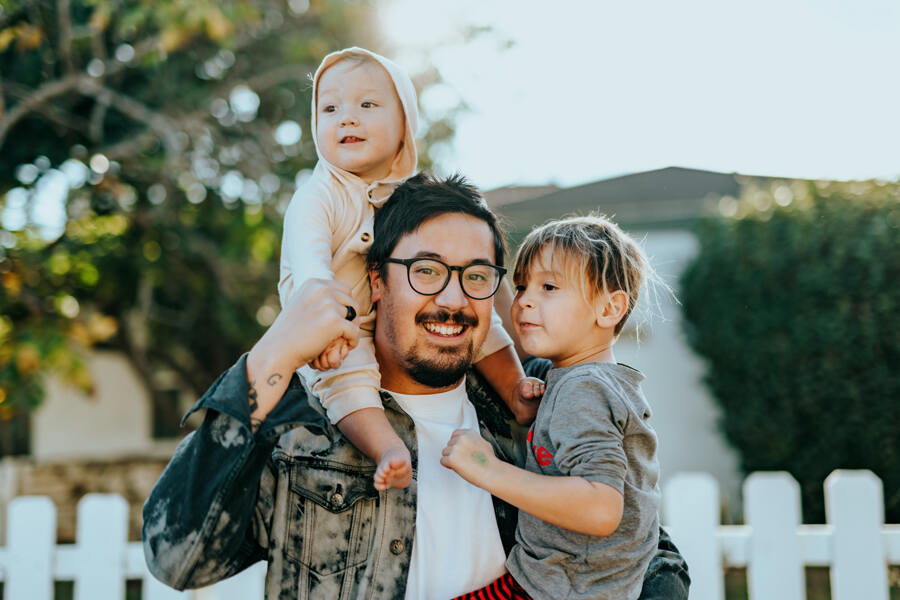 Männliche lächelnde Person mit zwei Kindern auf dem Arm und auf den Schultern sitzend