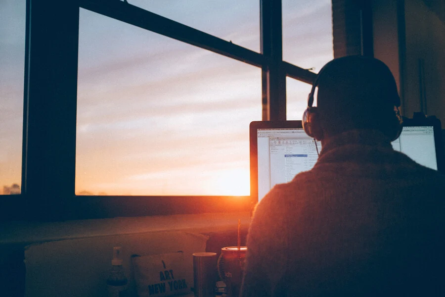 Ein Mann sitz im Sonnenuntergang vor einem Laptop und hat ein Headset auf