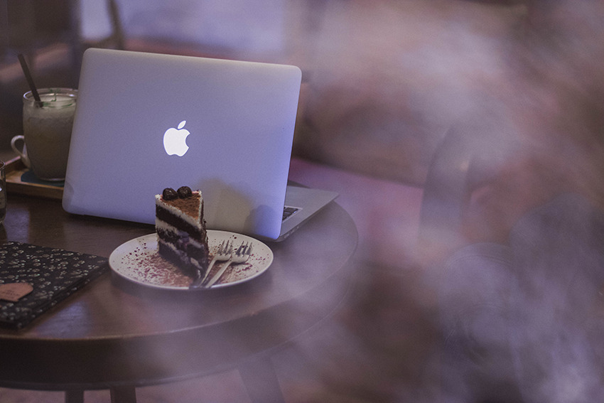 Auf einem Tisch steht ein Macbook und ein Stück Torte